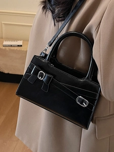 Chic black glossy handbag with bow detail and silver buckles worn with a wool coat