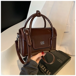 Close-up of dark brown glossy patent leather bag with silver metal logo and handle detail