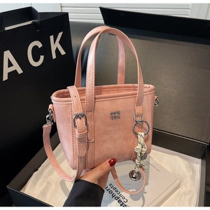 Close-up of pink bucket bag with woven bell charm and adjustable strap on black gift box