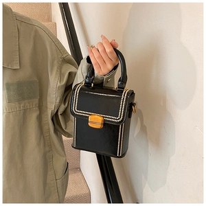 Detail of a vintage-style black patent leather box bag with gold beaded trim and clasp