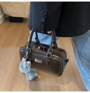 Detail of dark brown leather barrel bag with silver hardware and bow charm accessory