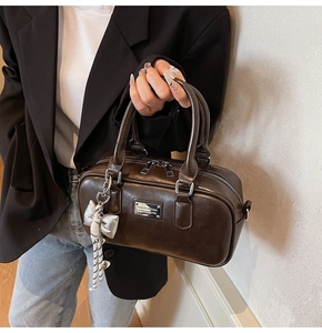 Close-up of chocolate brown bowling bag with silver bow charm and double zipper detail