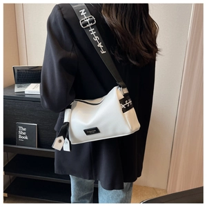 Detail of white lychee leather pillow bag featuring a wide 'FASHION' printed shoulder strap