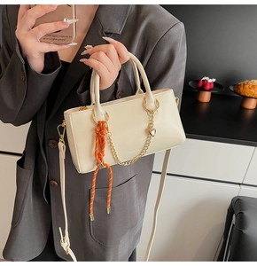 Détail du sac à main en cuir blanc cassé avec chaîne dorée et pendentif tissé orange