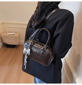 Deep brown glossy leather bowling bag with bow charm shown as a stylish underarm bag