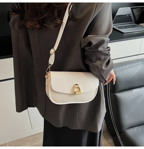 Detail view of cream crossbody bag featuring a golden arch buckle and woven texture