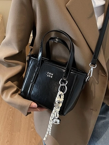 Chic black patent leather bucket bag with white lettering and woven pendant charm