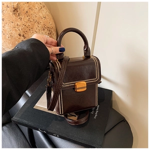 Close-up of a vintage dark brown box bag with gold rivet details and top handle