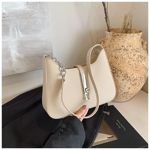 Close-up of beige woven underarm bag with silver bar lock on a lifestyle backdrop