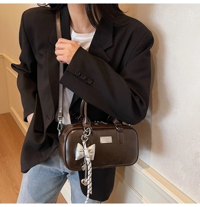Detail shot of a dark brown Boston bag with a silver bow charm and adjustable strap