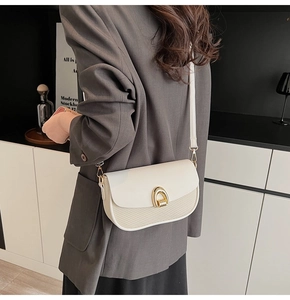 Detail of minimalist beige crossbody bag featuring a gold U-shaped buckle and woven texture