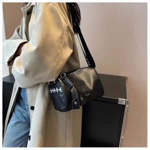 Model wearing a black pebbled leather crossbody bag with a branded wide shoulder strap
