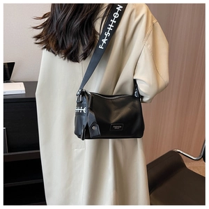 Close-up of black leather crossbody bag with wide FASHION letter strap on a model
