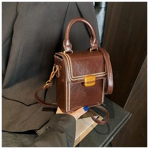 Detailed view of dark brown box bag featuring glossy leather texture and golden clasp