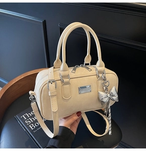 Chic cream bowling bag with silver bow charm on a black leather seat close-up