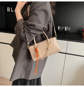 Détail du sac à main beige en cuir ciré avec chaîne métallique et pendentif tissé orange