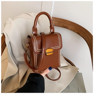 Detail of retro brown box bag featuring gold stud trim and metal lock closure