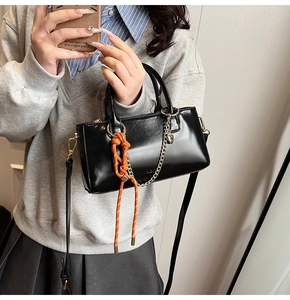 Détail d'un sac à main en cuir noir avec chaîne dorée et nœud tressé orange vif