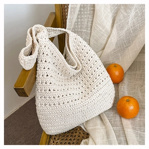 Dettaglio della borsa tote in crochet crema con trama a maglia su una sedia di legno