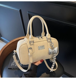 Detail of cream bowling handbag with ribbon and silver bow charm on a chair