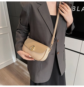 Detail of beige woven crossbody bag featuring a golden horseshoe metal clasp and leather flap