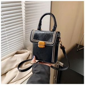 Detail of black leather box bag featuring golden metal studs and rectangular swivel lock