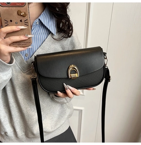 Close-up of black crossbody bag featuring woven texture and gold horseshoe twist lock
