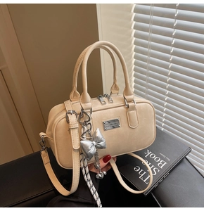 Detailed view of beige bowling bag featuring silver bow charm and textured leather