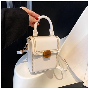 Detailed close-up of white leather box bag featuring gold studs and metal buckle closure