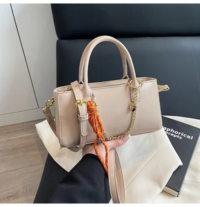 Détail du sac beige en cuir ciré avec chaîne coeur dorée et décoration en corde tressée orange