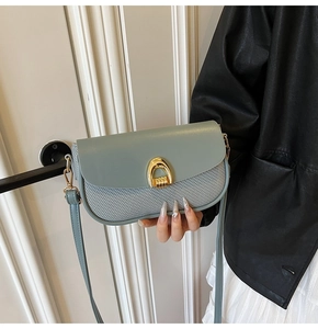 Detail of light blue crossbody bag with gold horseshoe buckle and woven texture texture