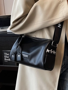 Chic black pebbled leather cylinder crossbody bag with wide logo strap worn on beige coat