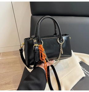 Détail du sac à main noir en cuir ciré avec chaîne dorée et pendentif en corde orange
