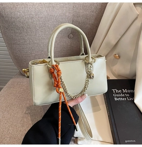 Détail du sac à main beige avec chaîne dorée et breloque en corde orange sur chaise