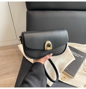 Detail of black leather crossbody bag with golden horseshoe buckle and woven texture