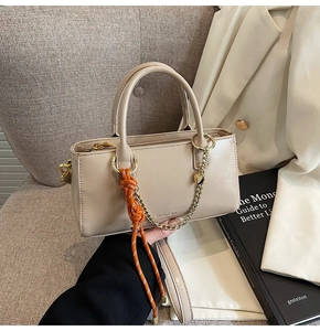 Détail du sac à main beige en cuir ciré avec chaîne en cœur dorée et corde orange vive