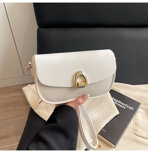 Close-up of white semi-circle flap bag with golden horseshoe buckle and textured fabric