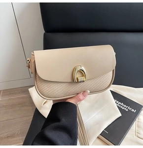Close-up of minimalist beige leather and woven handbag with gold horseshoe buckle clasp