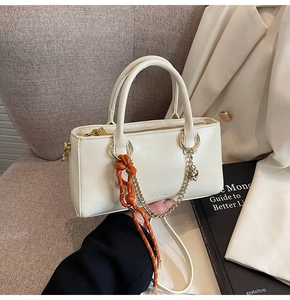 Détail du sac à main en cuir crème avec breloque cœur et sangle tissée sur canapé