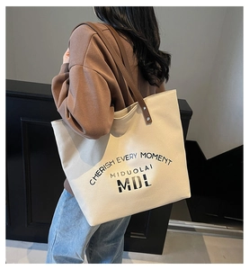 Detail of a large beige canvas tote bag with brown leather straps worn by a model