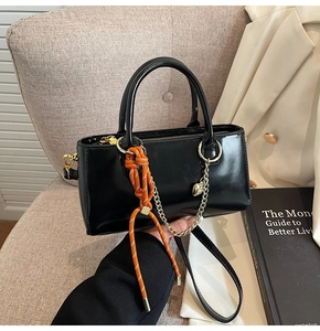 Détail du sac à main en cuir verni noir avec nœud en corde orange et breloque en chaîne