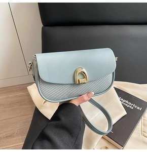 Detail of light blue crossbody bag featuring mixed textures and a gold horseshoe buckle