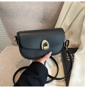 Detail of black saddle bag featuring smooth leather flap, woven texture, and gold U-buckle