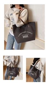 Detail of dark grey canvas tote bag with brown leather handles and artistic lettering