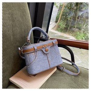 Detail of blue denim box bag featuring brown leather trim and metal buckle accents