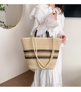 Detail of woven straw tote bag with black stripes and dual straps for summer travel