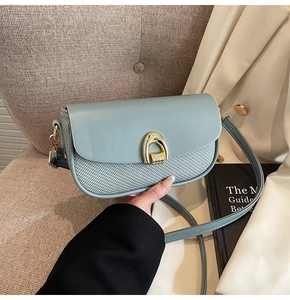 Detail of light blue square bag with woven texture and golden horseshoe metal clasp