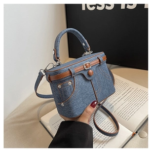 Detailed view of denim box bag with jean-style stitching and brown leather handles