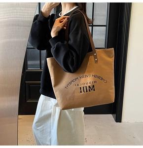 Detail shot of a tan canvas tote bag with brown leather straps worn by a model