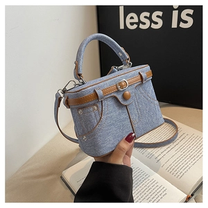 Close-up of light blue denim mini box bag with brown leather trim and silver metal rivets